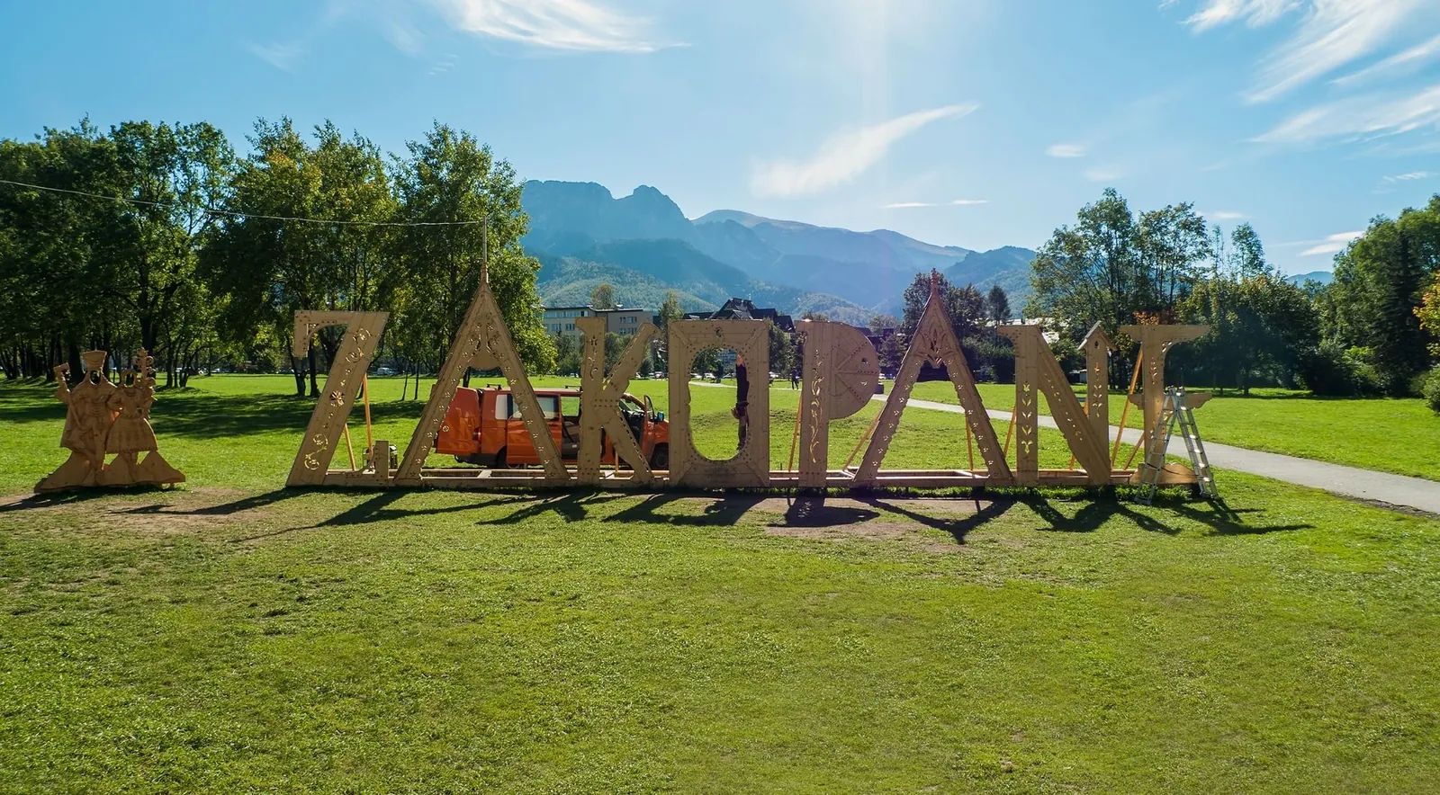Large wooden ZAKOPANE letters on a summer lawn with a mountain ridge behind