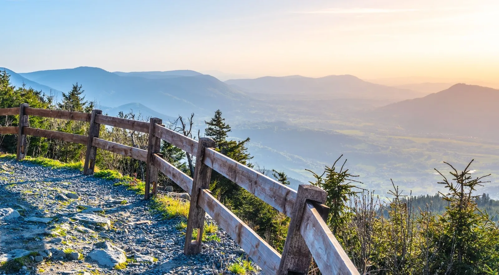 A wooden-fenced hilltop viewpoint over forested foothills at golden hour