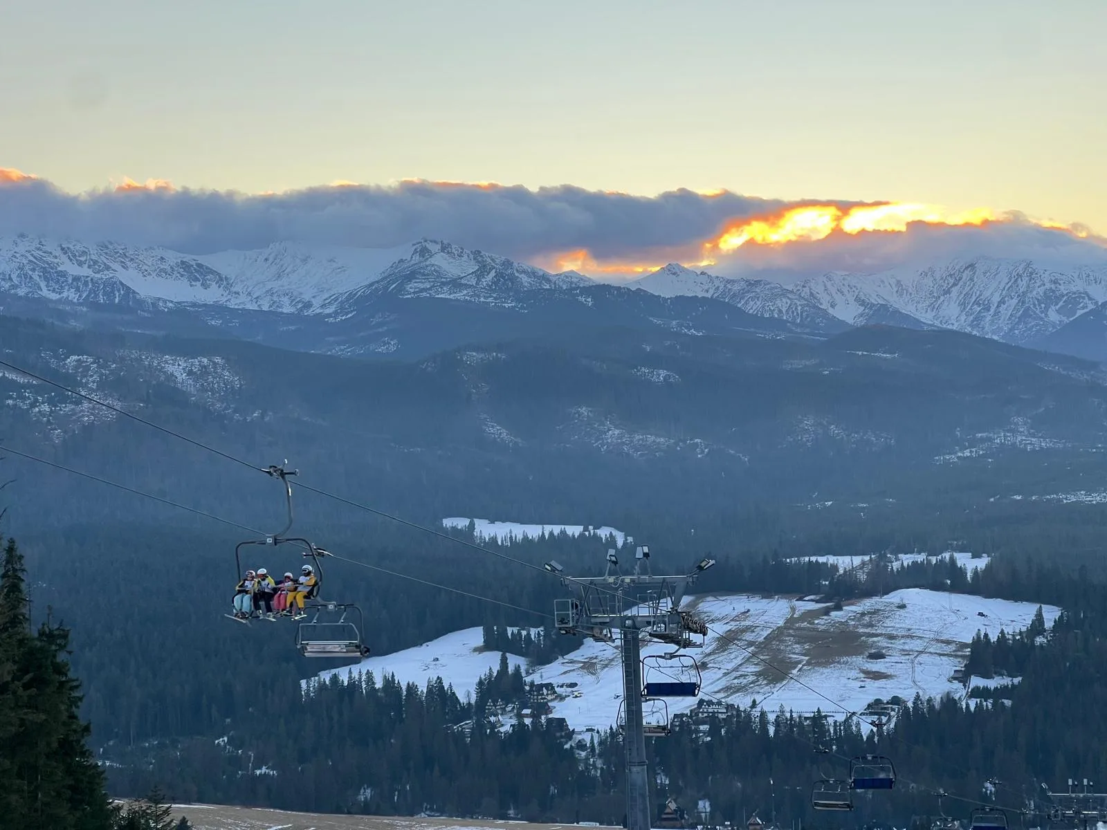 Skiers on a chairlift with snowy Tatra peaks and sunset clouds
