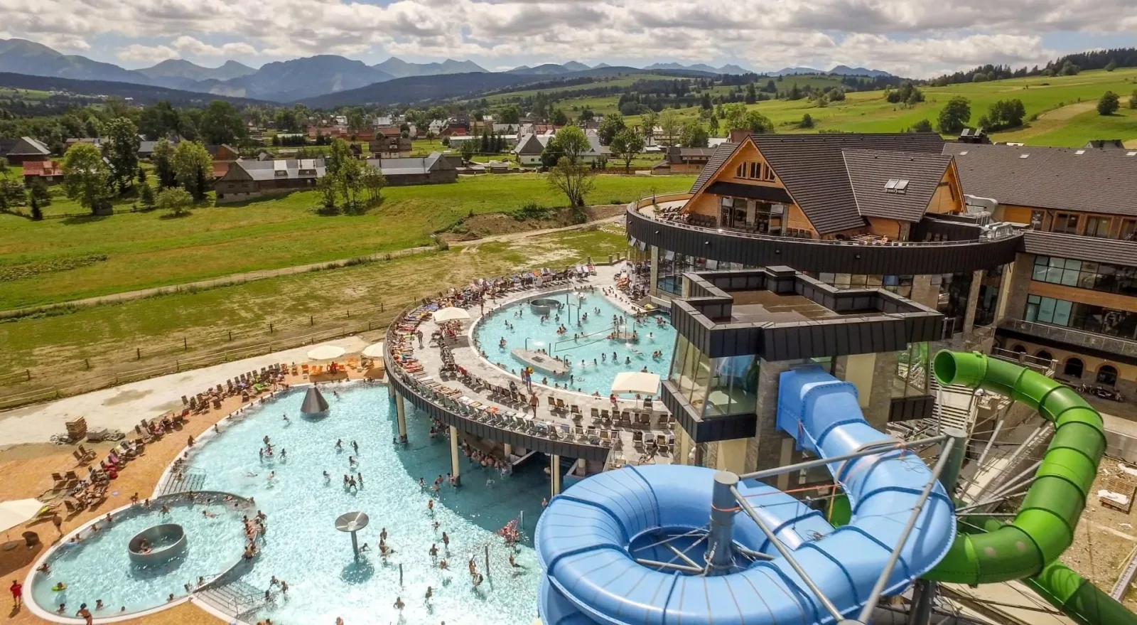 Aerial view of outdoor pools, sunbeds and water slides with mountains behind