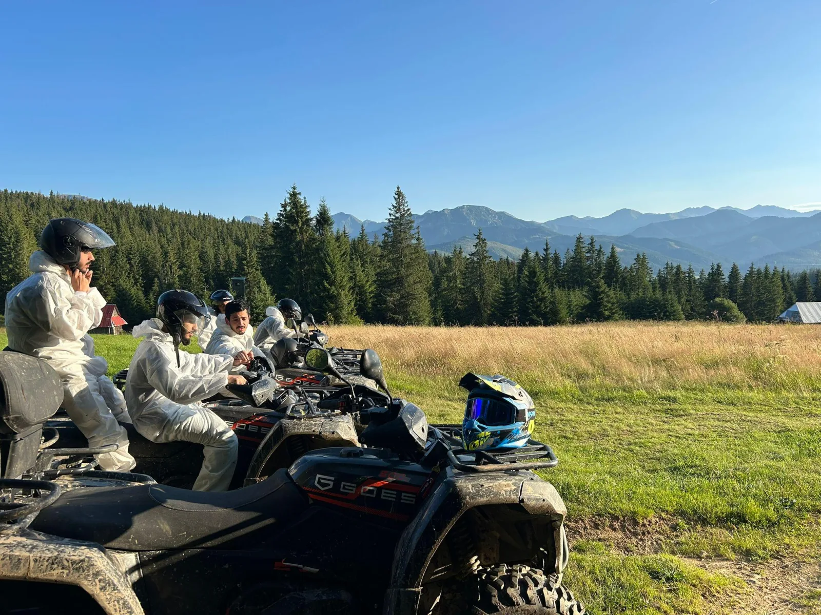 Riders in white overalls on quads looking out toward the mountains