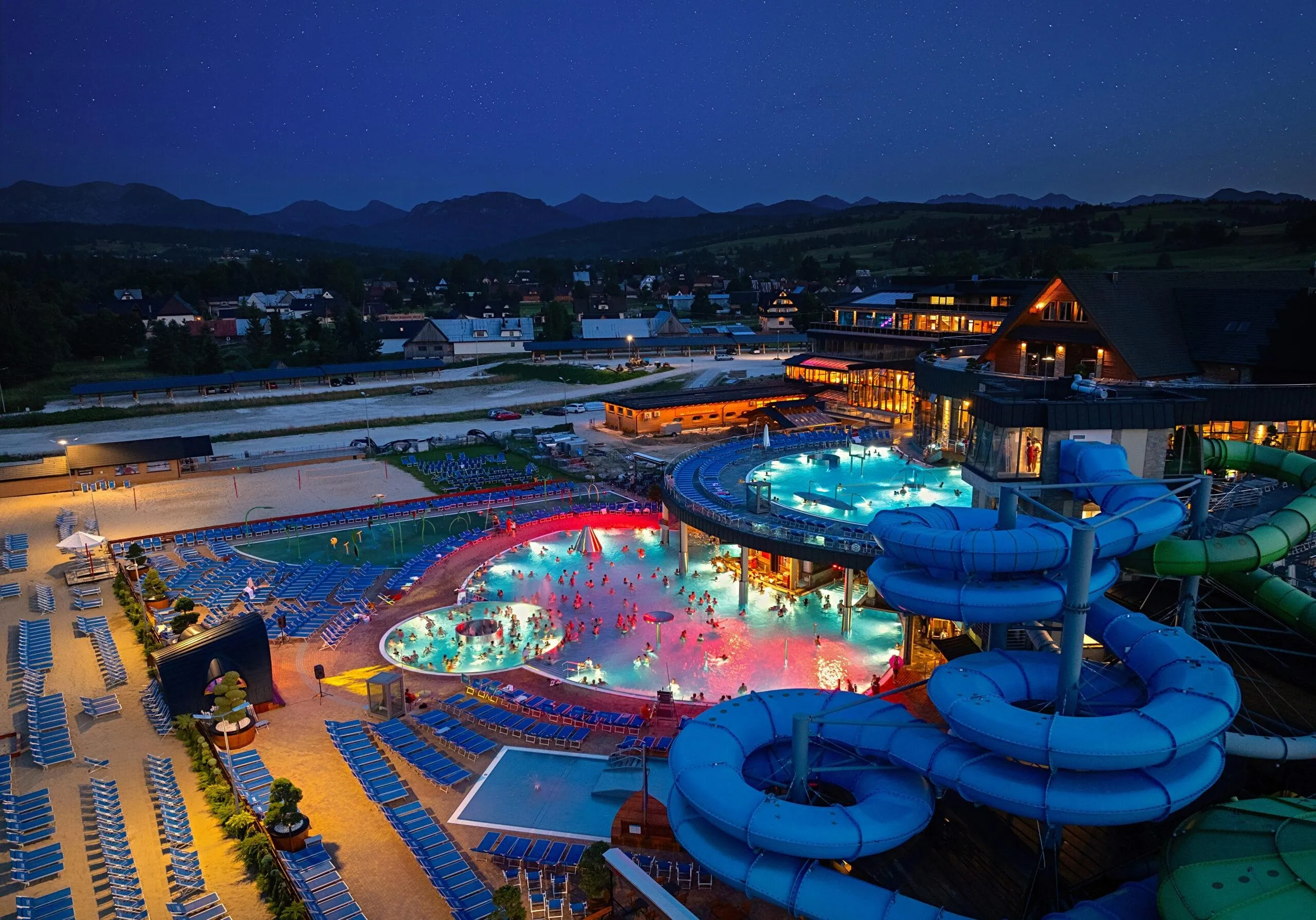 Thermal pool complex lit up at dusk with outdoor pools and water slides