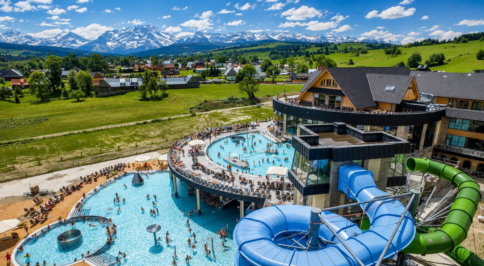 Aerial view of outdoor thermal pools and water slides with snowy peaks