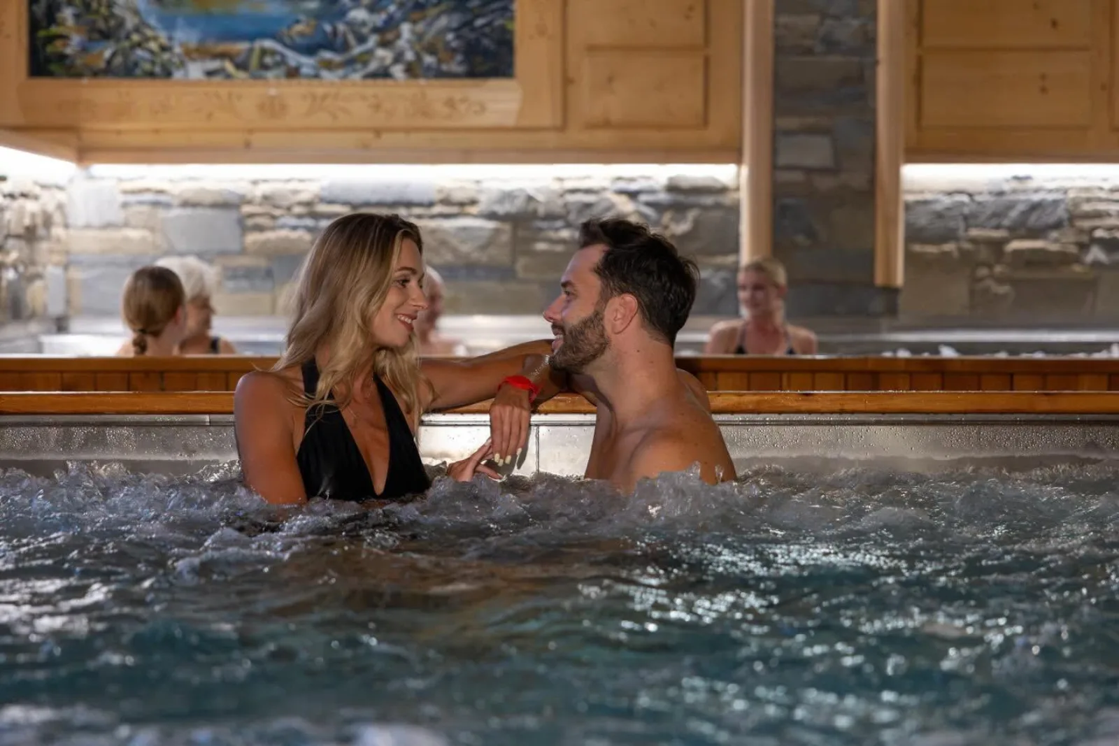 Couple chatting in a bubbling indoor jacuzzi with wooden panelling