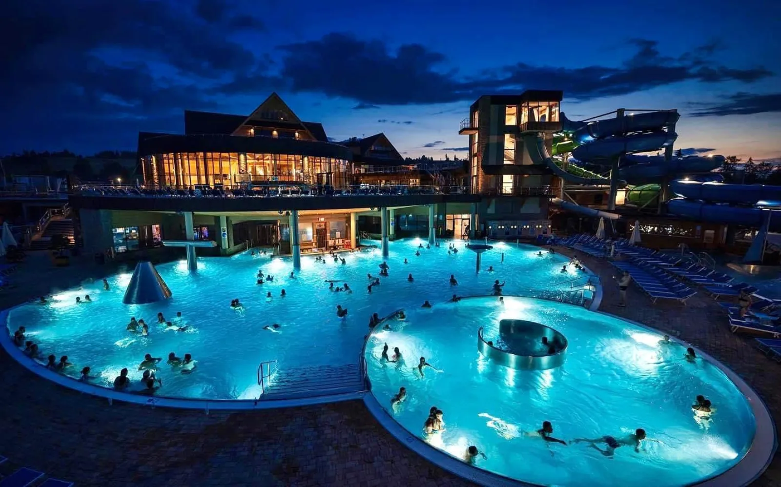 Floodlit outdoor thermal pools and water slides at dusk