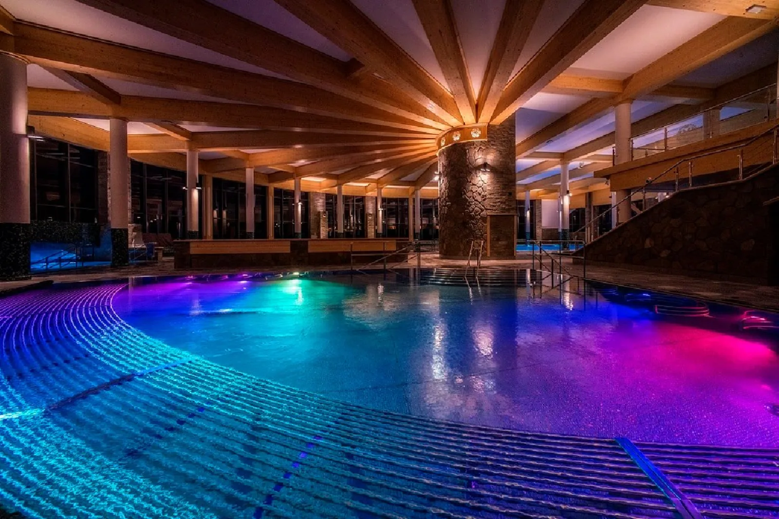 Indoor pool lit purple and blue under a radiating timber roof