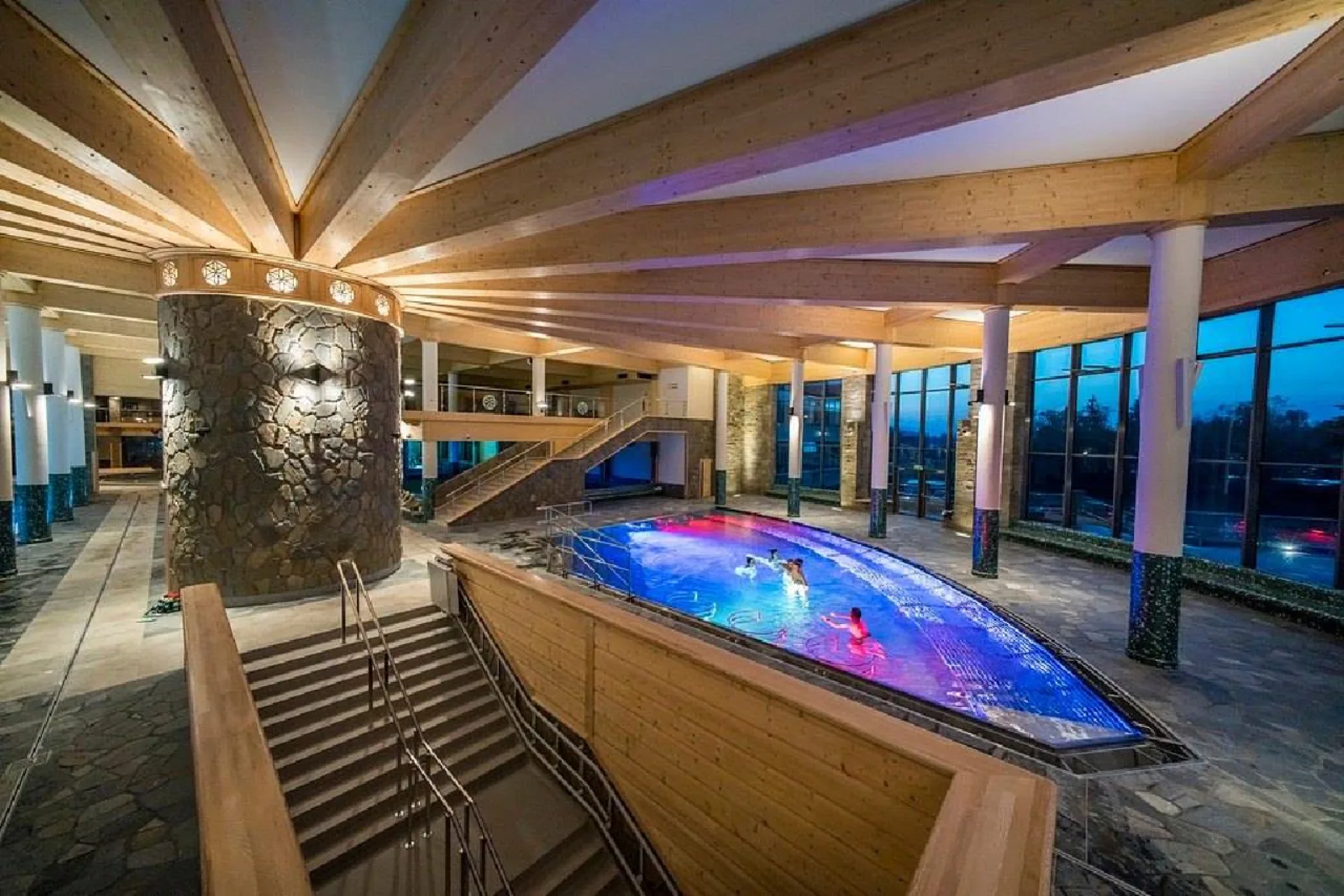 Indoor pool with swimmers seen from wooden stairs under timber beams