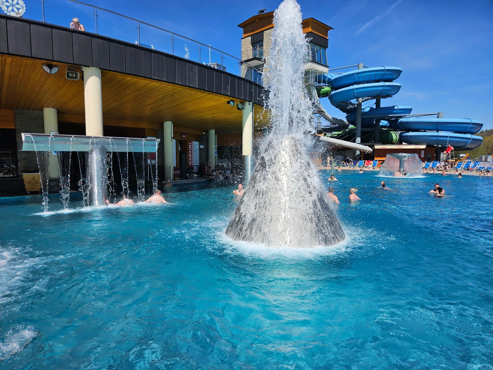 Water cone fountain and waterfall jets beside blue spiral water slides