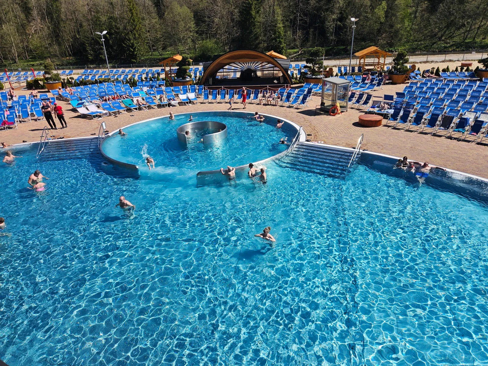 Round outdoor pool with a central ring, blue sunbeds and a stage