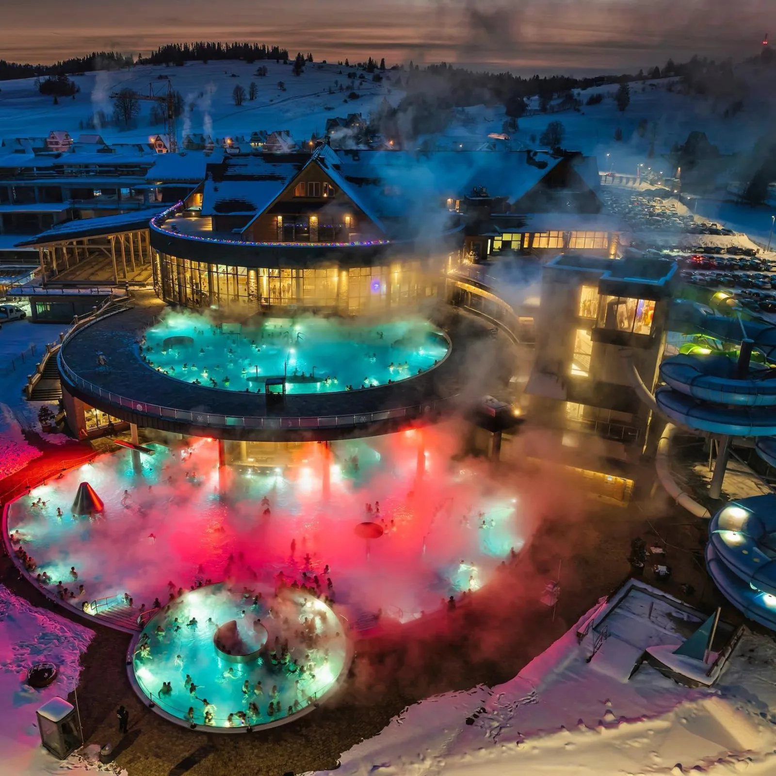 Aerial view of steaming lit pools surrounded by snow at dusk