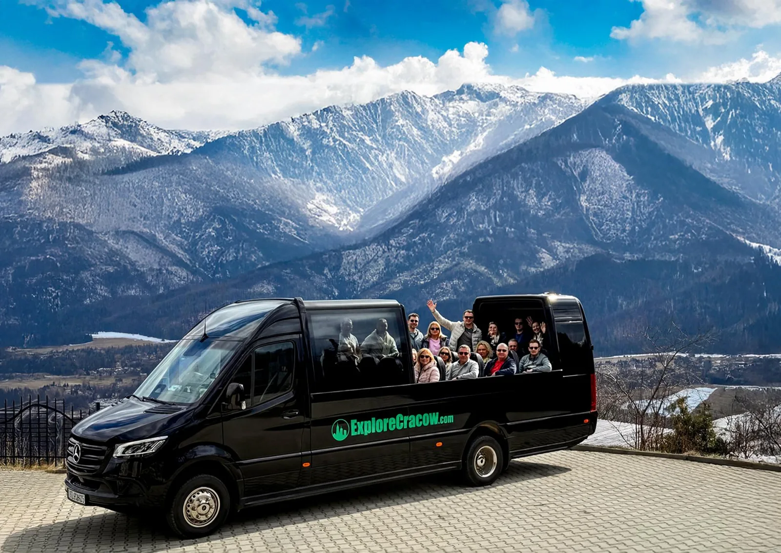 Group waving from an open-top minibus with snowy mountains behind