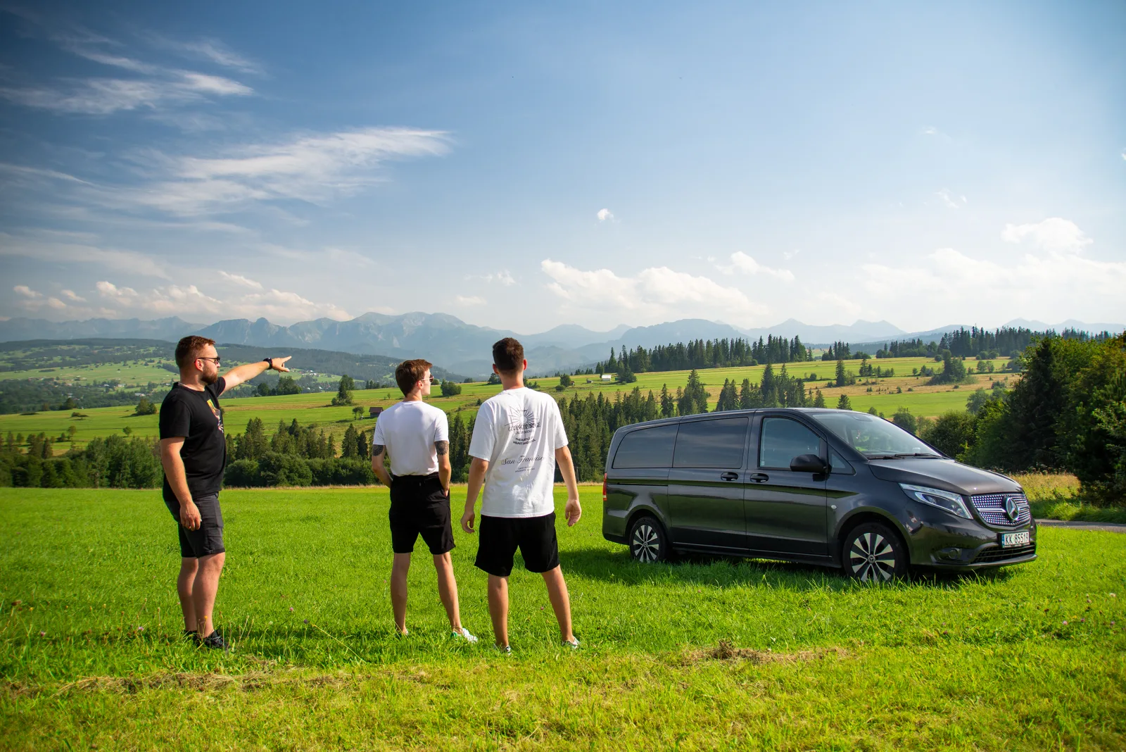 Guide pointing out distant mountains beside a parked black van