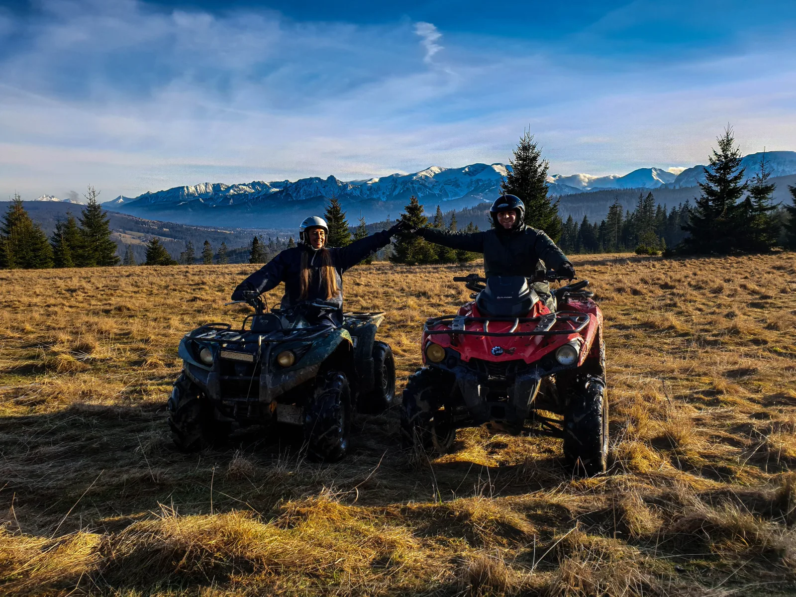 Two riders on quads in a dry meadow below snowy Tatra peaks