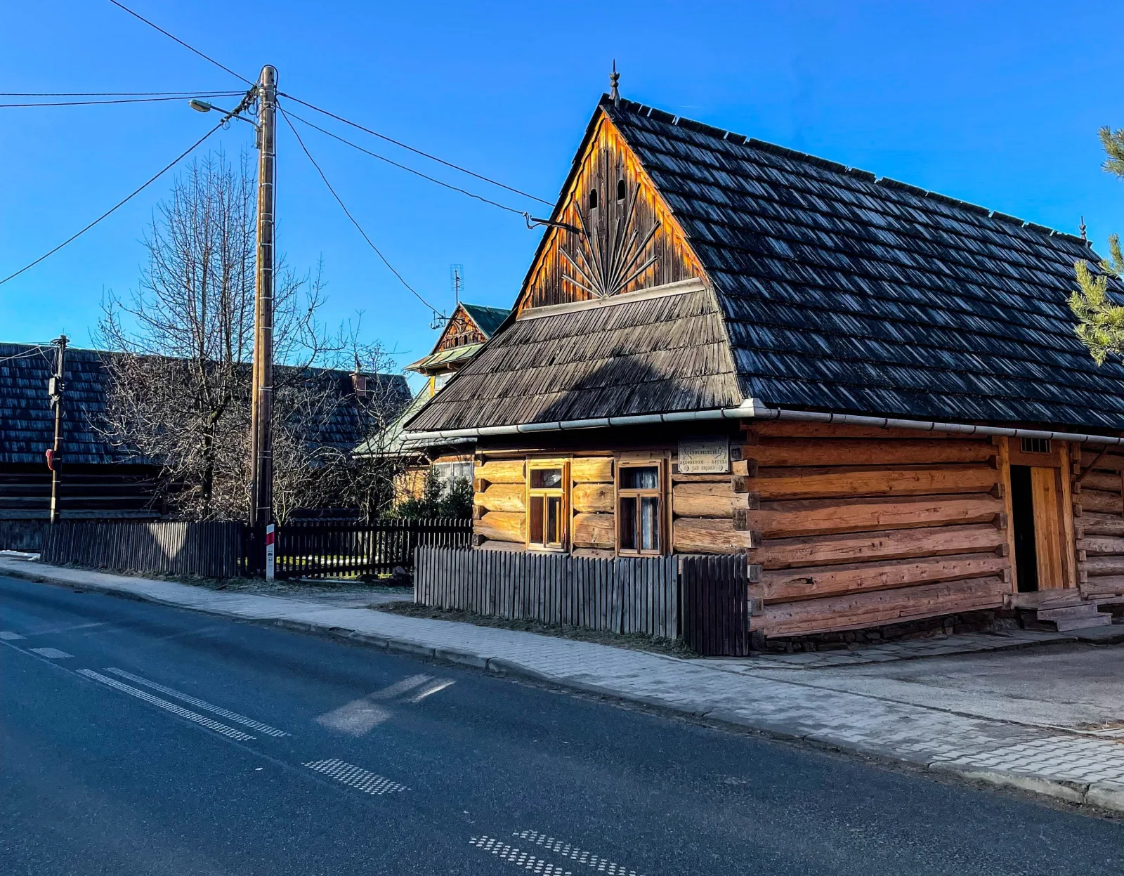 Old log house with a shingled roof beside a village road