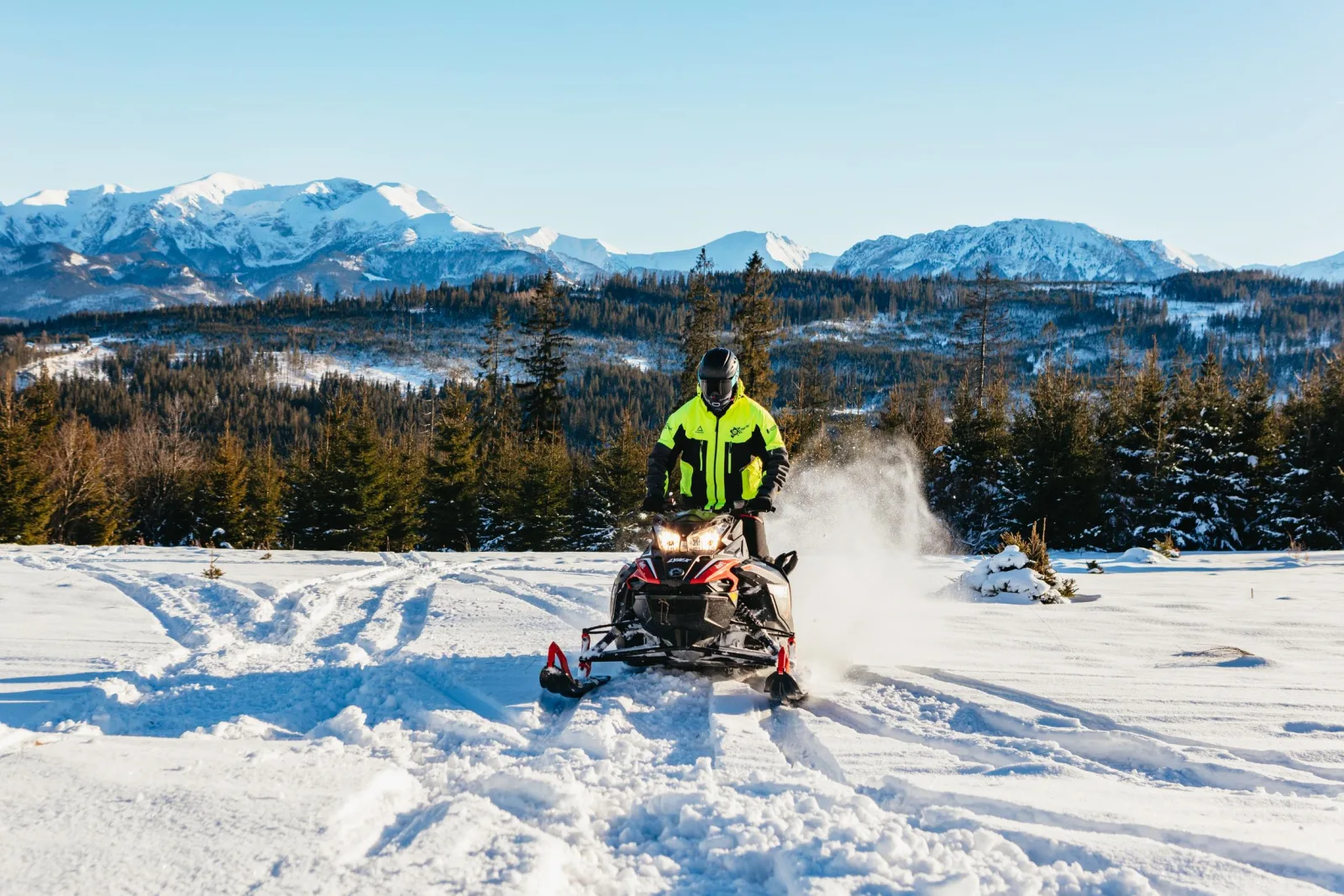 Rider in a hi-vis jacket driving a snowmobile across fresh snow