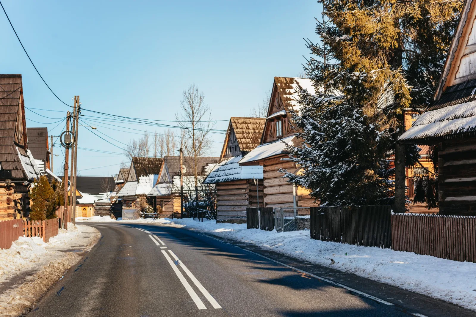 Road lined with wooden log houses and snow on a sunny day