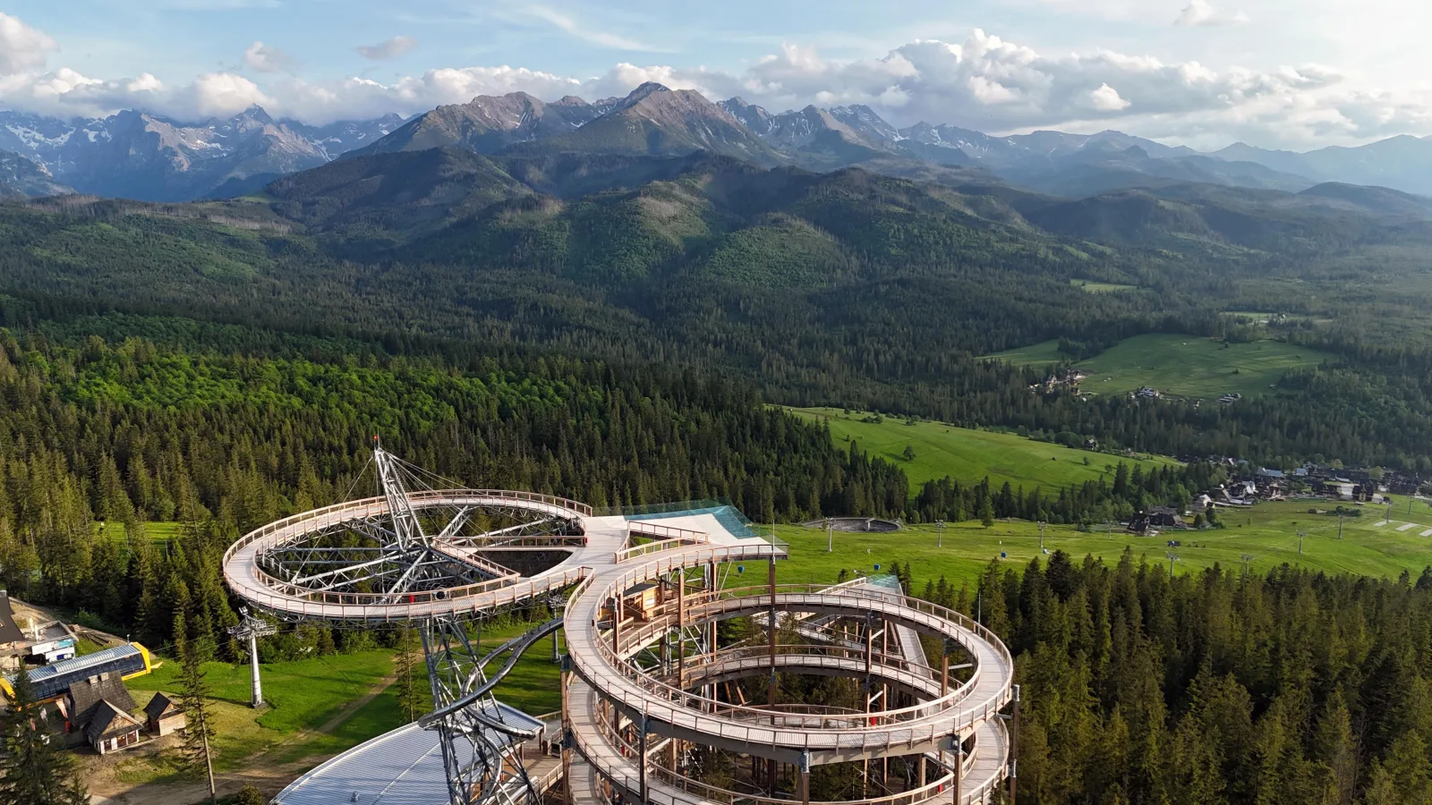 Aerial view of a looping wooden viewing tower above forest and mountains