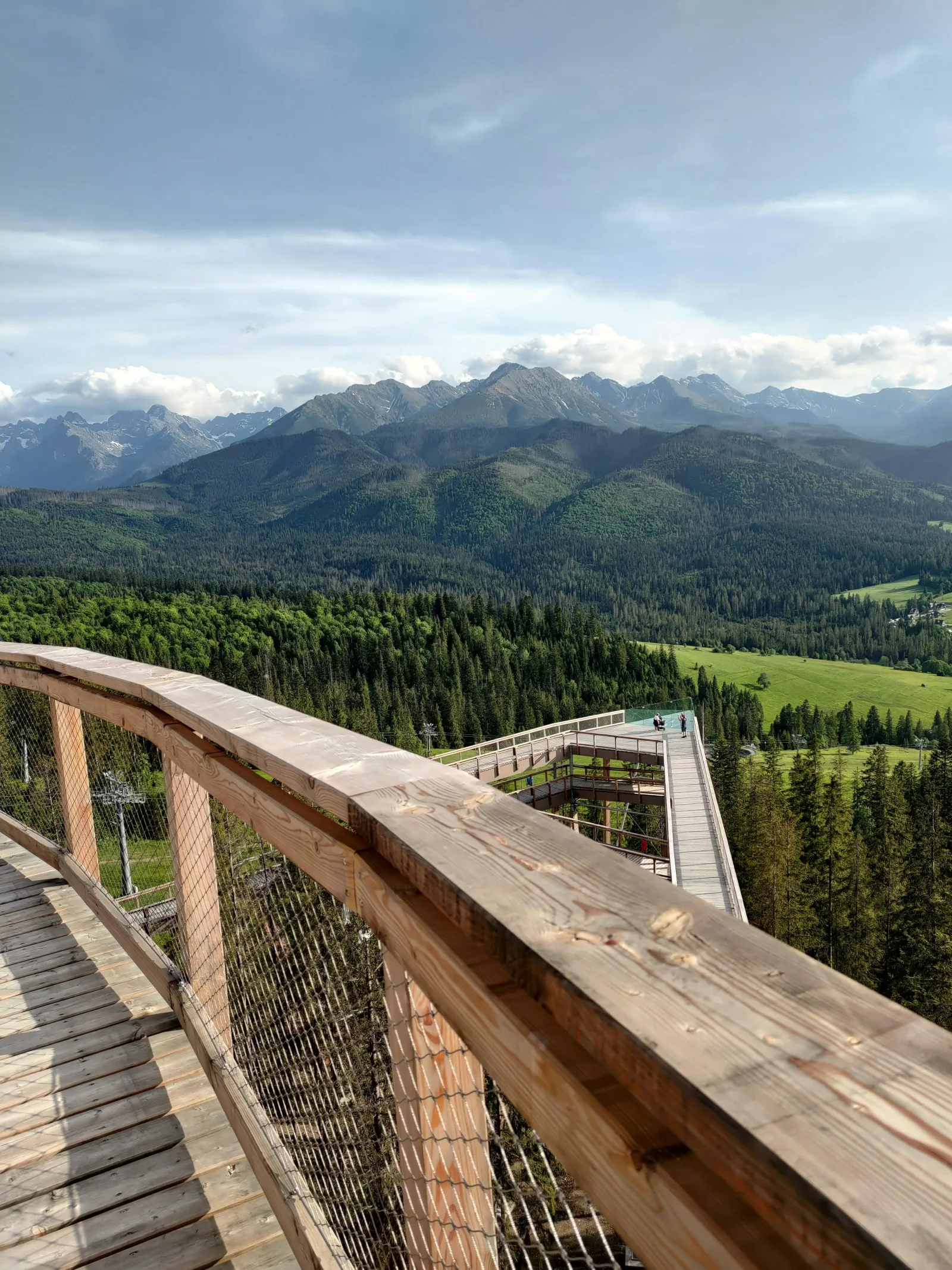 Wooden walkway railing with a wide view over forest to the Tatras