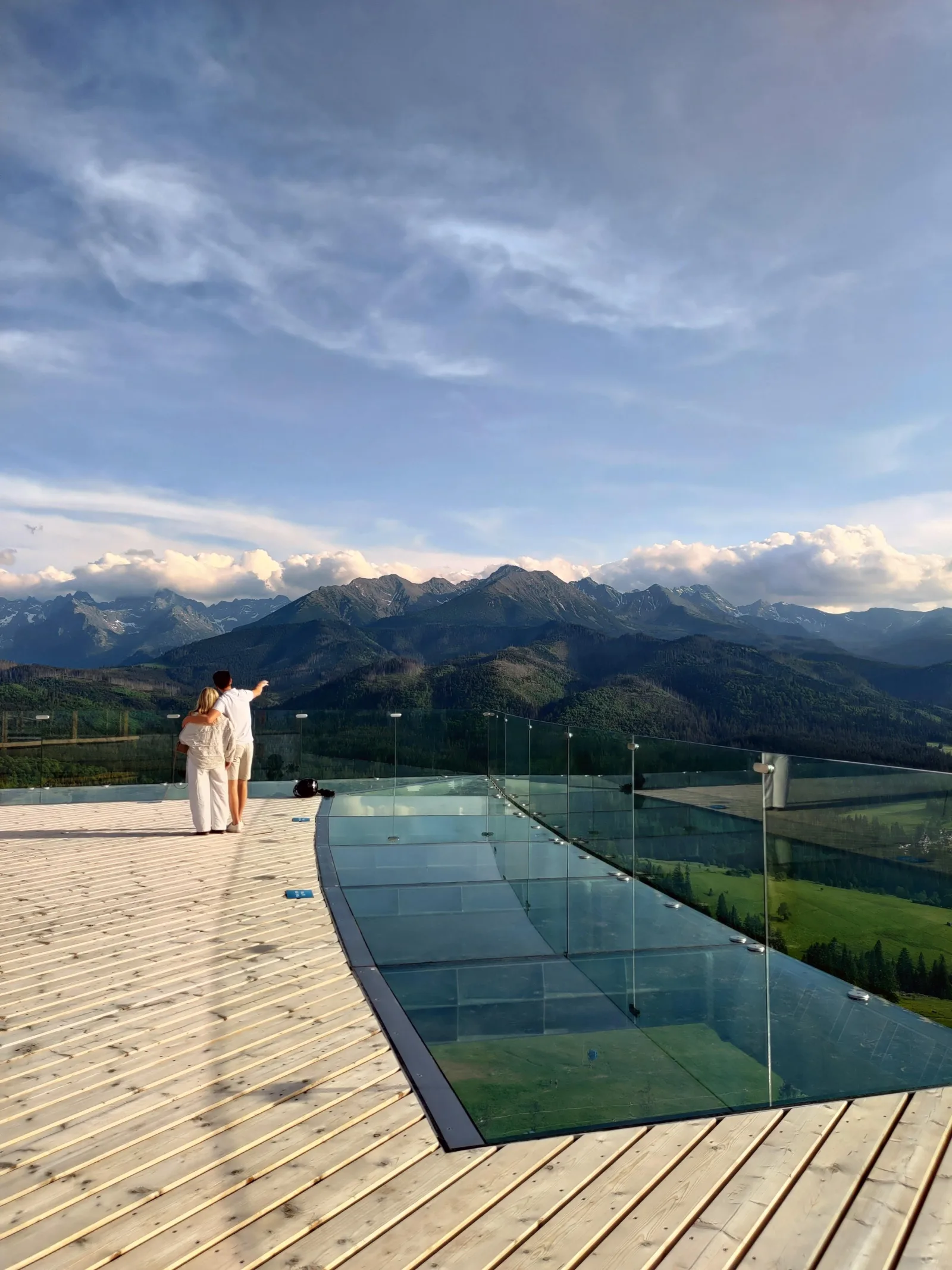 Couple on a viewing deck with a glass floor facing the mountains
