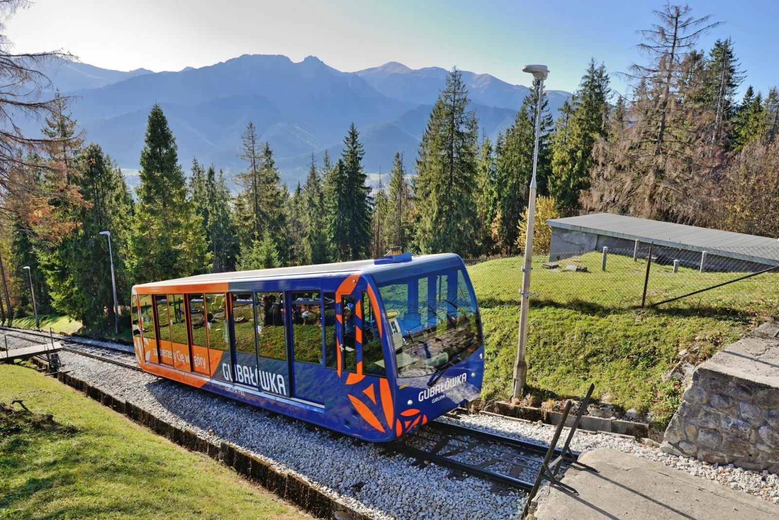 Blue and orange Gubałówka funicular car among autumn trees and mountains