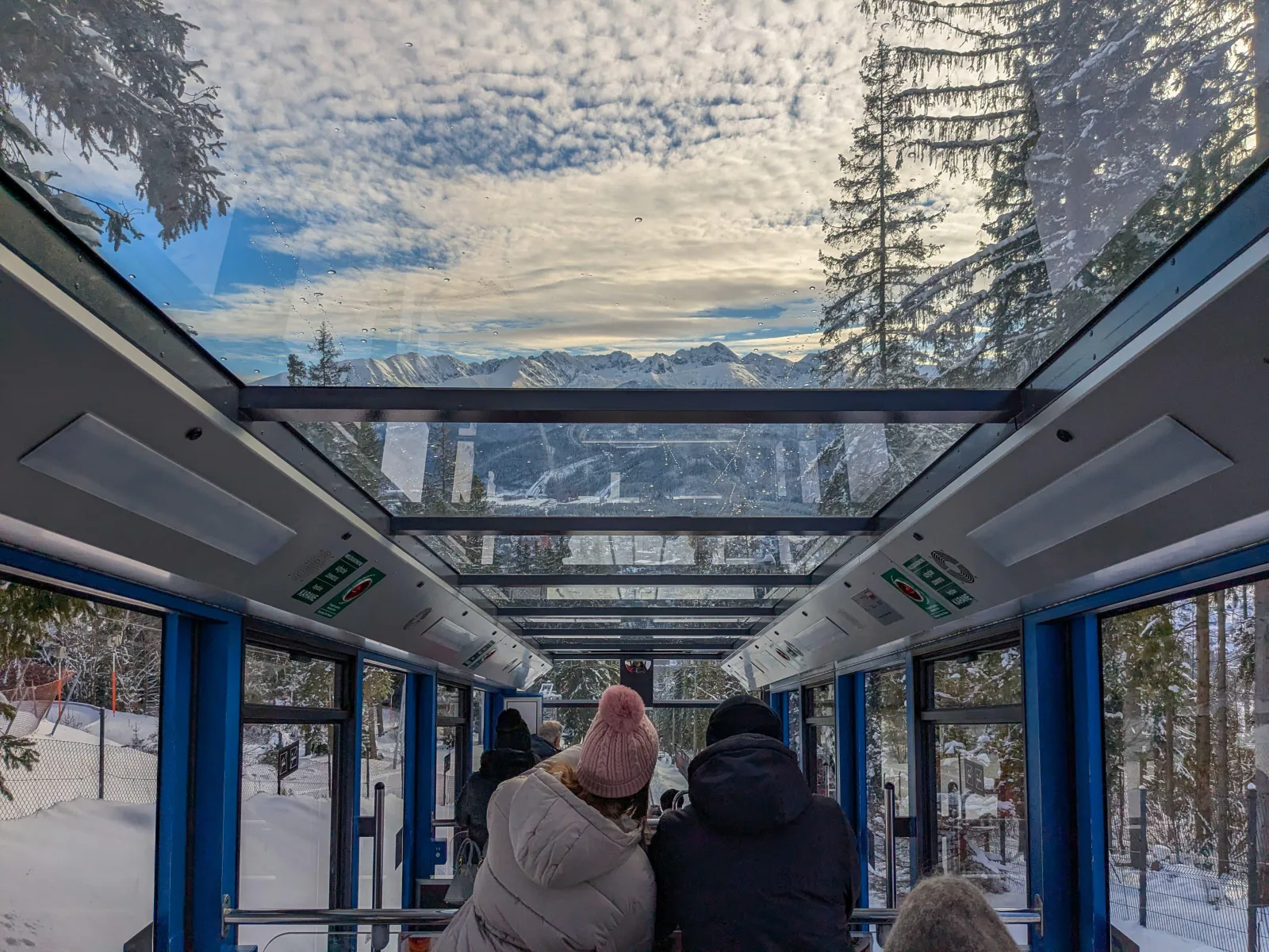 Passengers inside a glass-roofed funicular car looking out at snowy peaks