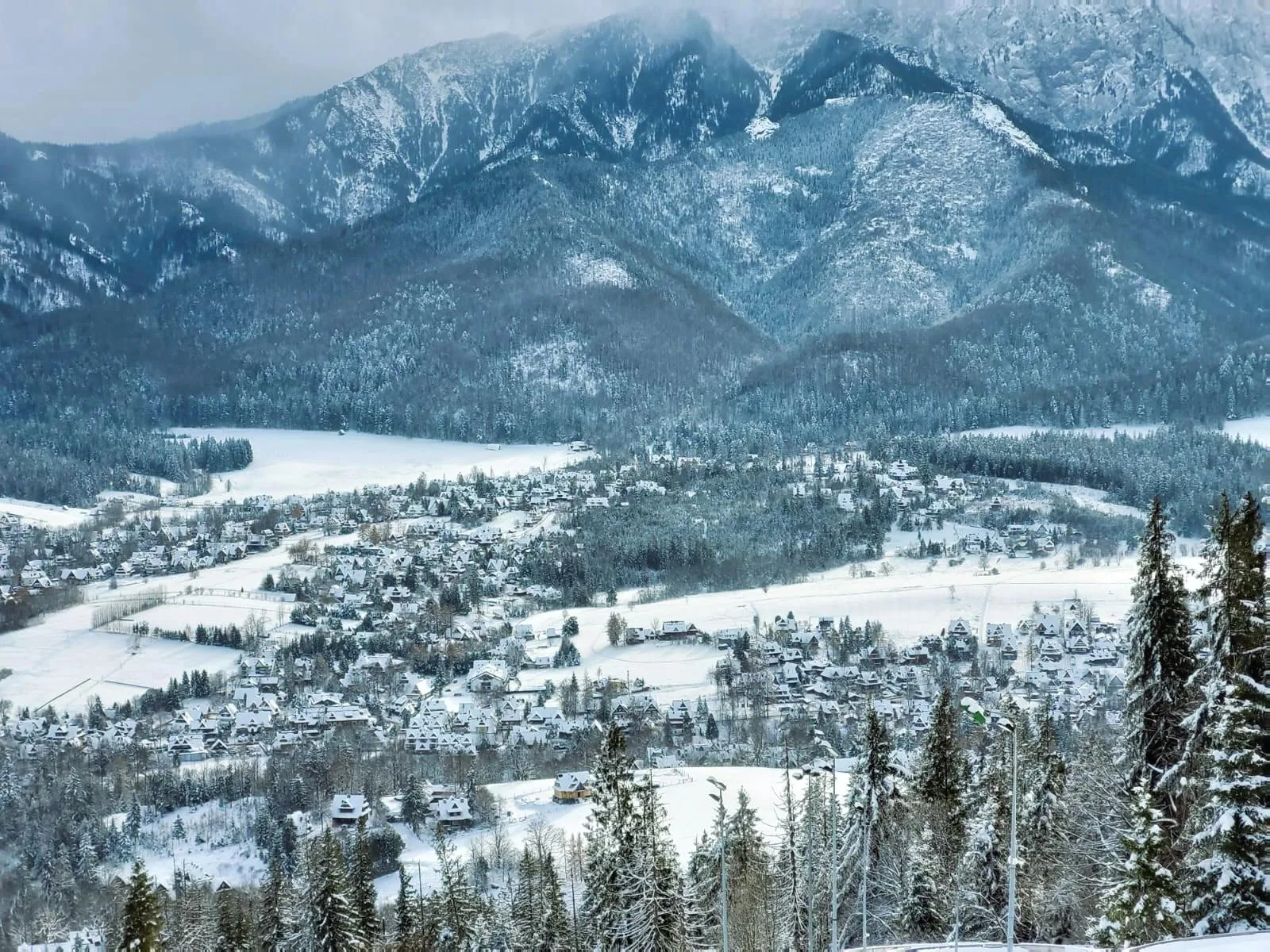Snow-covered valley of houses below a forested mountain ridge