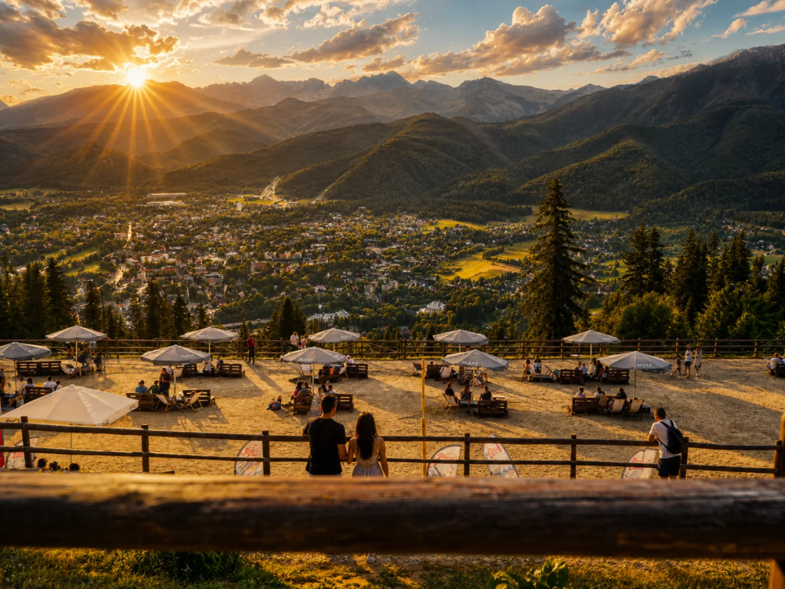Hilltop terrace with umbrellas overlooking Zakopane and mountains at sunset