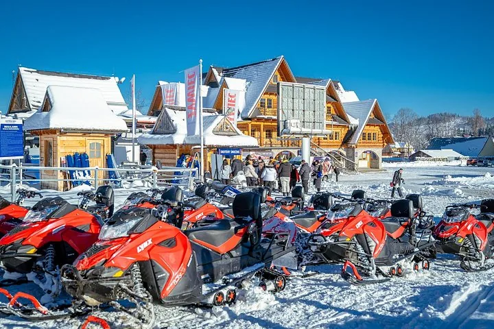 Rows of red snowmobiles parked in front of wooden highlander buildings