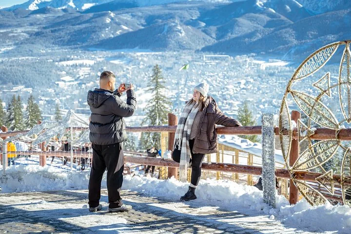 Visitors taking photos at a snowy railing above Zakopane and the mountains