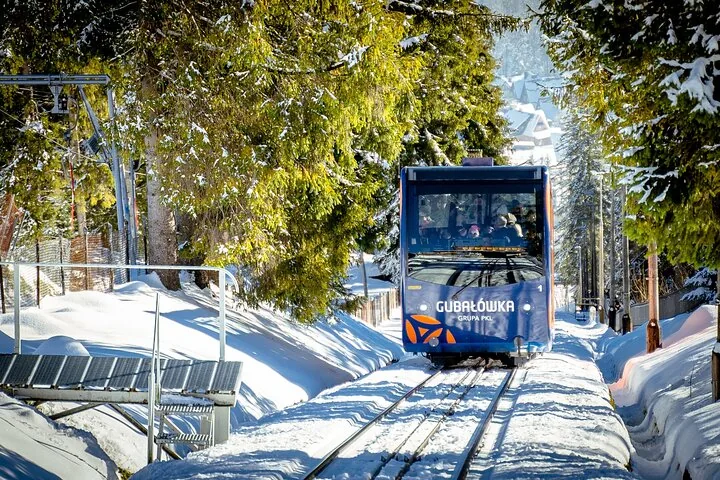 Blue Gubałówka funicular car on a snow-lined track between pine trees