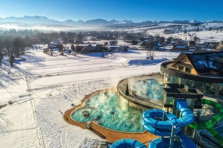 Outdoor thermal pools with blue water slides and snowy mountains behind