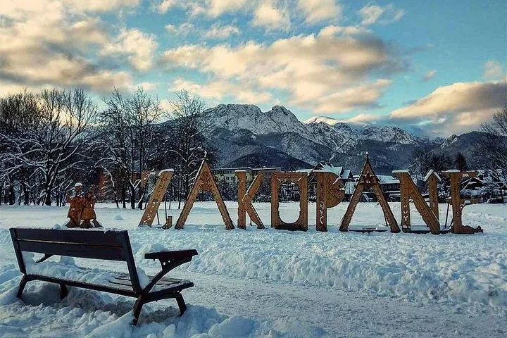 Large wooden Zakopane letters standing in snow below mountain peaks