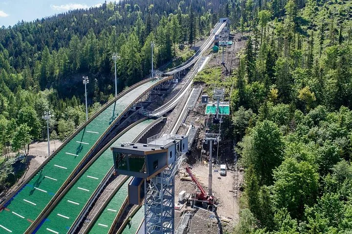 Aerial view of ski jumps with green landing slopes in a forest