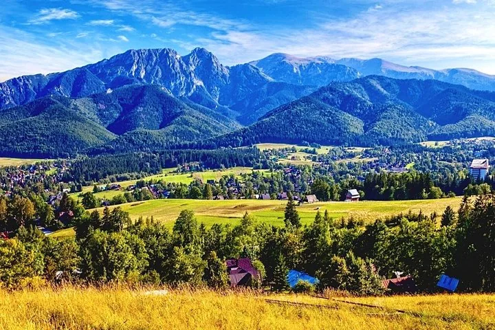 Meadows and houses below a rocky mountain ridge in summer