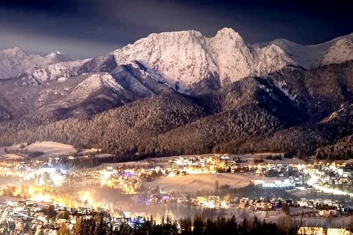 Town lights at night below snow-covered mountain peaks