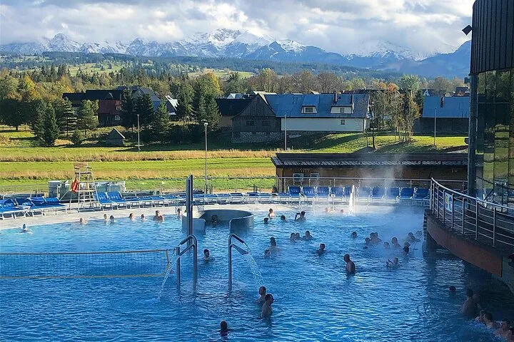 Steam rising from an outdoor thermal pool with snow-capped peaks beyond