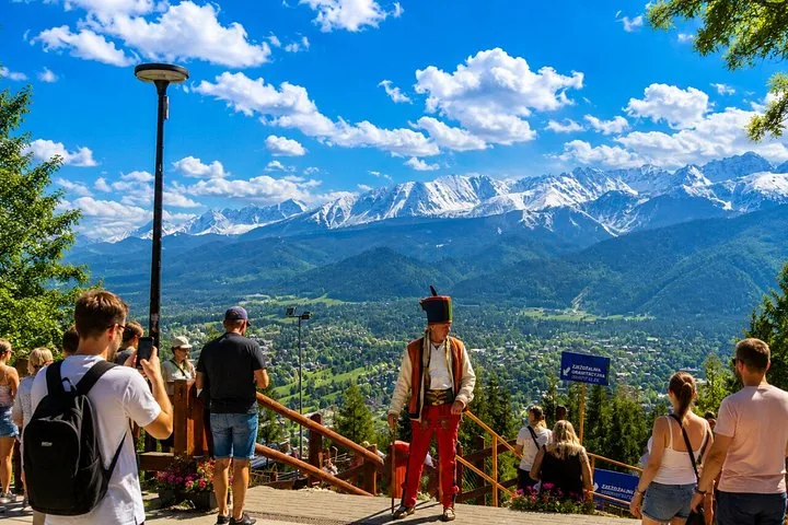 Visitors and a man in highland dress at a viewpoint over snowy peaks