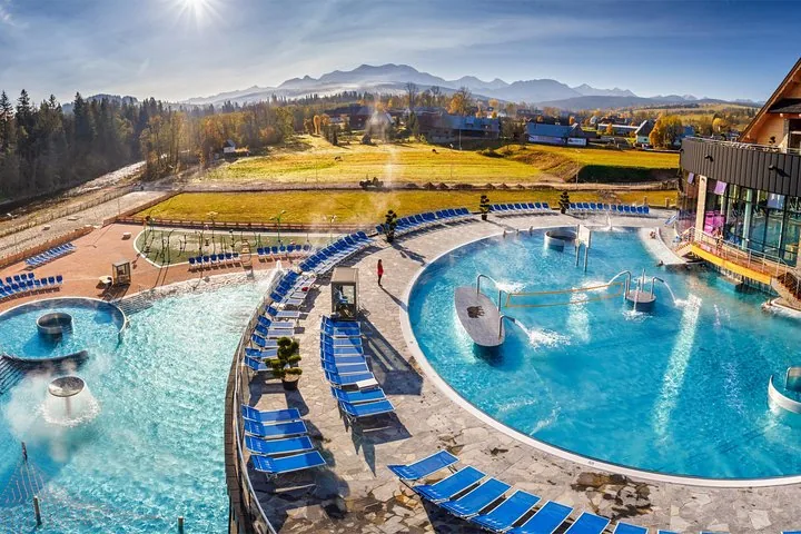 Outdoor thermal pools and blue sunbeds under a low sun with mountains