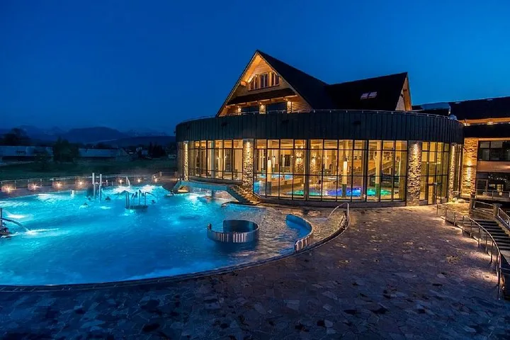 Outdoor pool lit blue at dusk beside a round glass hall