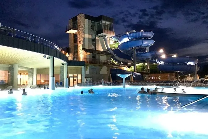 Floodlit outdoor pool at night with blue spiral water slides