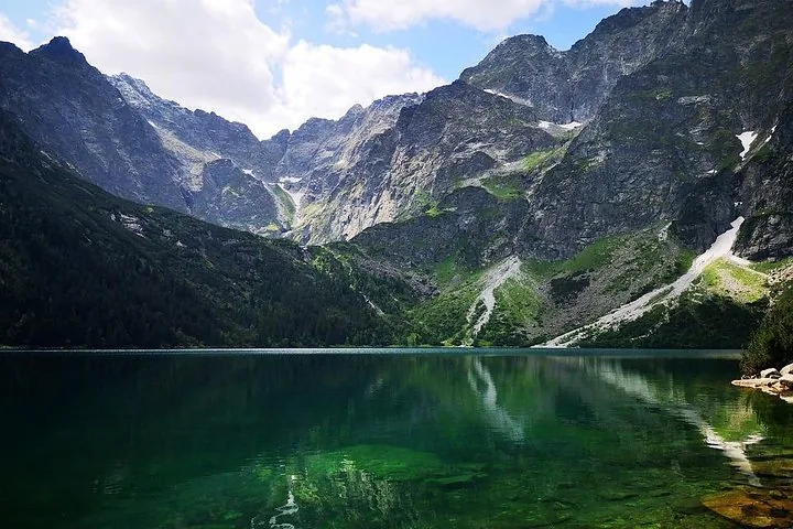 Calm lake reflecting steep grey mountain walls and snow patches