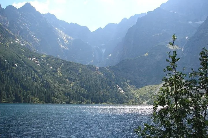 Sunlit mountain lake below forested slopes and grey rock walls