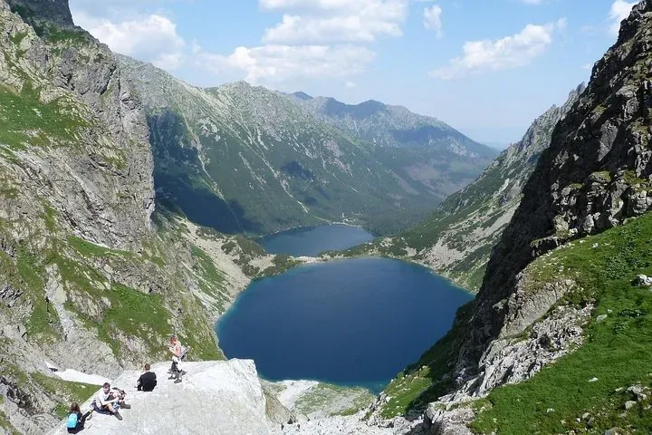 Hikers on rocks above a deep blue mountain lake between steep ridges