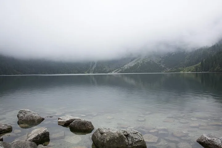 Mountain lake under low cloud with smooth boulders along the shore
