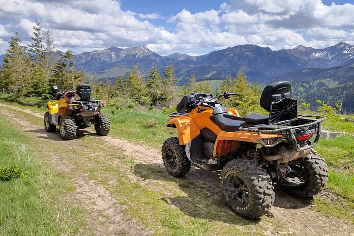Two orange ATVs parked on a dirt track below mountain ridges
